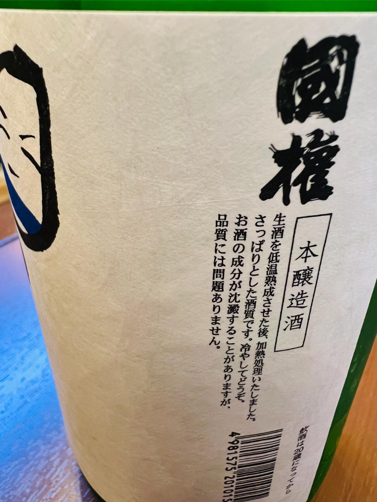 国権 本醸造 小法師の側面ラベル接写。低温熟成させた生酒を加熱処理した本醸造酒で、さっぱりとした酒質と冷やして楽しむ飲み方を紹介。成分が沈殿する場合があるものの品質には問題ない旨も記載されている。