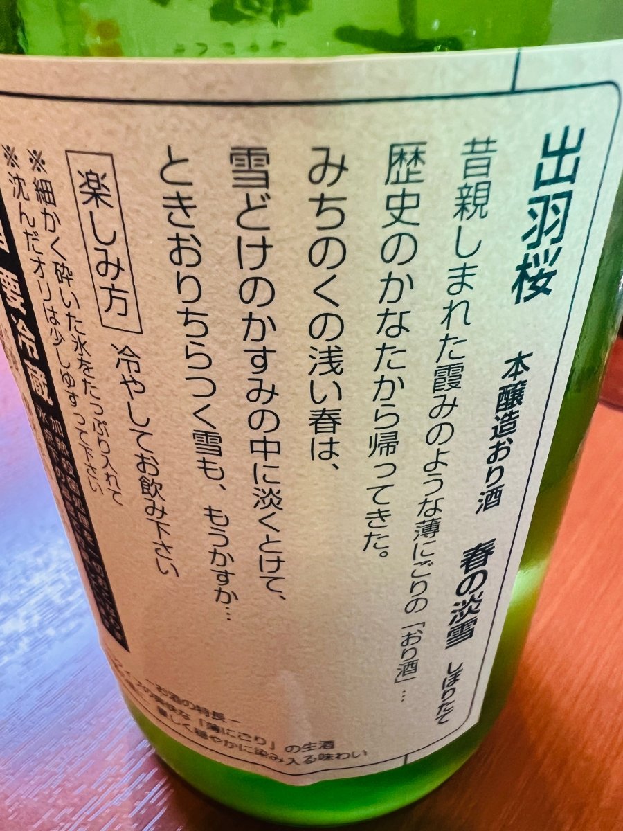 山形・出羽桜酒造「本醸造おり酒 春の淡雪」の裏ラベル詳細。昔親しまれた霞のような薄にごりの「おり酒」が、歴史のかなたから帰ってきたという叙情的なメッセージが記されています。みちのくの浅い春、雪どけのかすみの中に淡くとける情景を、繊細な「うすにごり」の生酒の味わいになぞらえた、情緒あふれるラベル画像です。