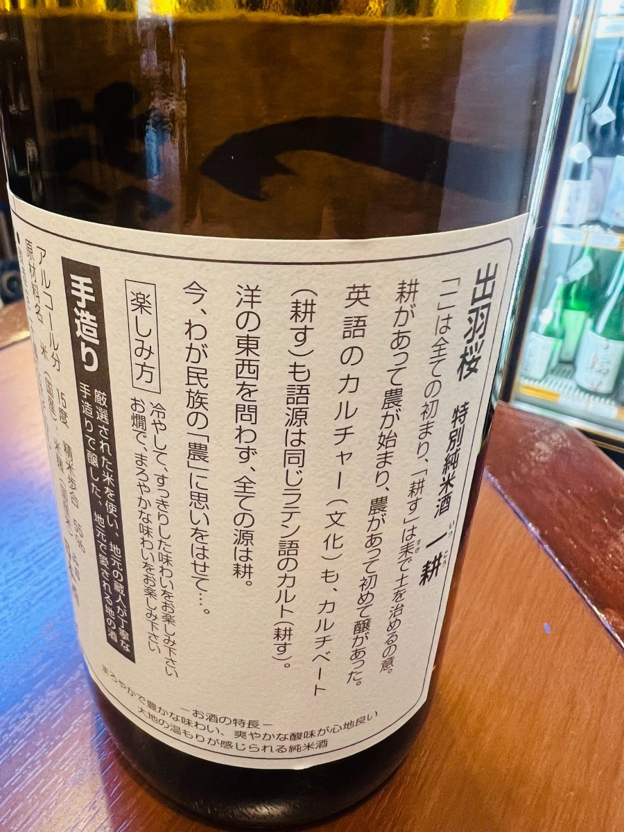 「出羽桜 特別純米酒 一耕」の裏面ラベル。英語の「カルチャー（文化）」と「カルチベート（耕す）」の語源が同じラテン語であることに触れ、全ての源は「耕」にあるという蔵の哲学が記されています。バナナやカスタードのような柔らかな香りと、お米本来の重層的な旨味を支える「農」への熱い思いが伝わる、製品情報の画像です。