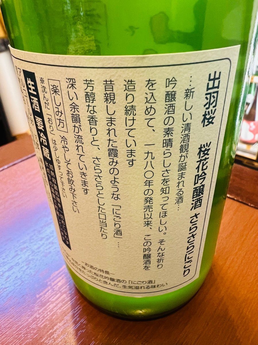 「出羽桜 桜花吟醸酒 さらさらにごり 本生」の裏面ラベル。1980年の発売以来、吟醸酒の素晴らしさを伝えたいという祈りを込めて造り続けられている歴史と、昔親しまれた霞のような「にごり酒」を現代に再現したストーリーが綴られています。芳醇な香りとさらさらとした口当たりの特徴や、沈んだ「おり」を少しゆすって冷やして楽しむ「楽しみ方」が記載された製品情報の画像です。