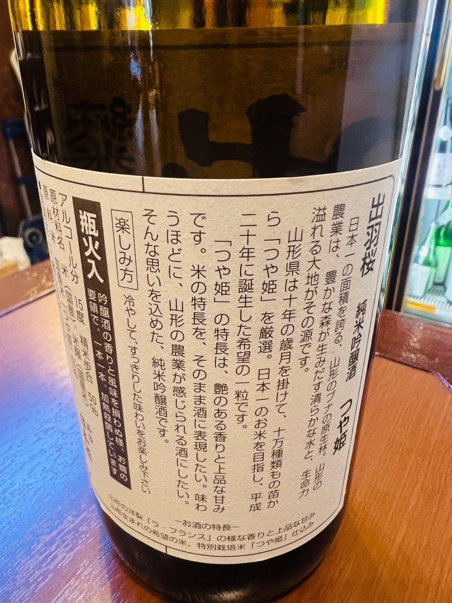 「出羽桜 純米吟醸 つや姫」の裏面ラベル。山形県が10万種類の苗から厳選した「つや姫」の特長である、艶のある香りと上品な甘みを表現した酒造りの背景が記されています。精米歩合50％、アルコール分15度といったスペックに加え、山形のブナの原生林が育む清らかな水への感謝が綴られた製品情報の画像です。
