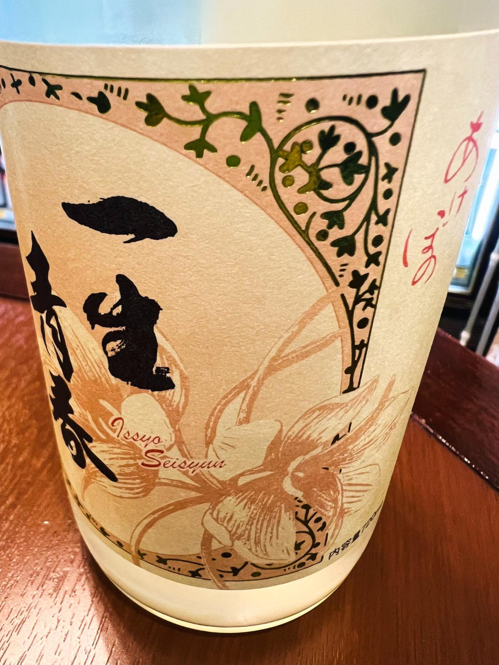 一生青春 特別純米 新酒おりがらみ本生 R8BYのラベル側面接写。淡い色合いのラベルに花柄と蔓模様が描かれ、「一生青春」の黒文字と「Issyo Seisyun」のローマ字表記が入ったデザイン。瓶の下部にはおりがらみ由来の白い濁りが見える。