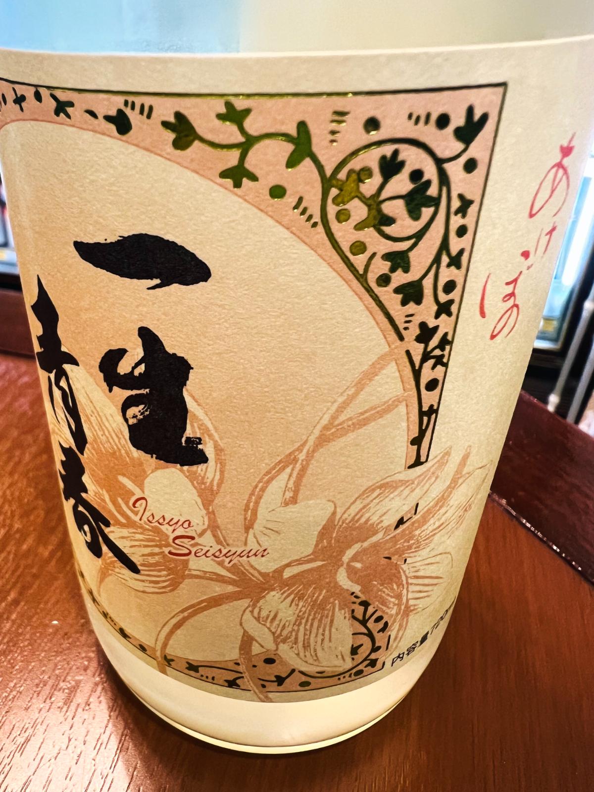 一生青春 特別純米 新酒おりがらみ本生 R8BYのラベル側面接写。淡い色合いのラベルに花柄と蔓模様が描かれ、「一生青春」の黒文字と「Issyo Seisyun」のローマ字表記が入ったデザイン。瓶の下部にはおりがらみ由来の白い濁りが見える。