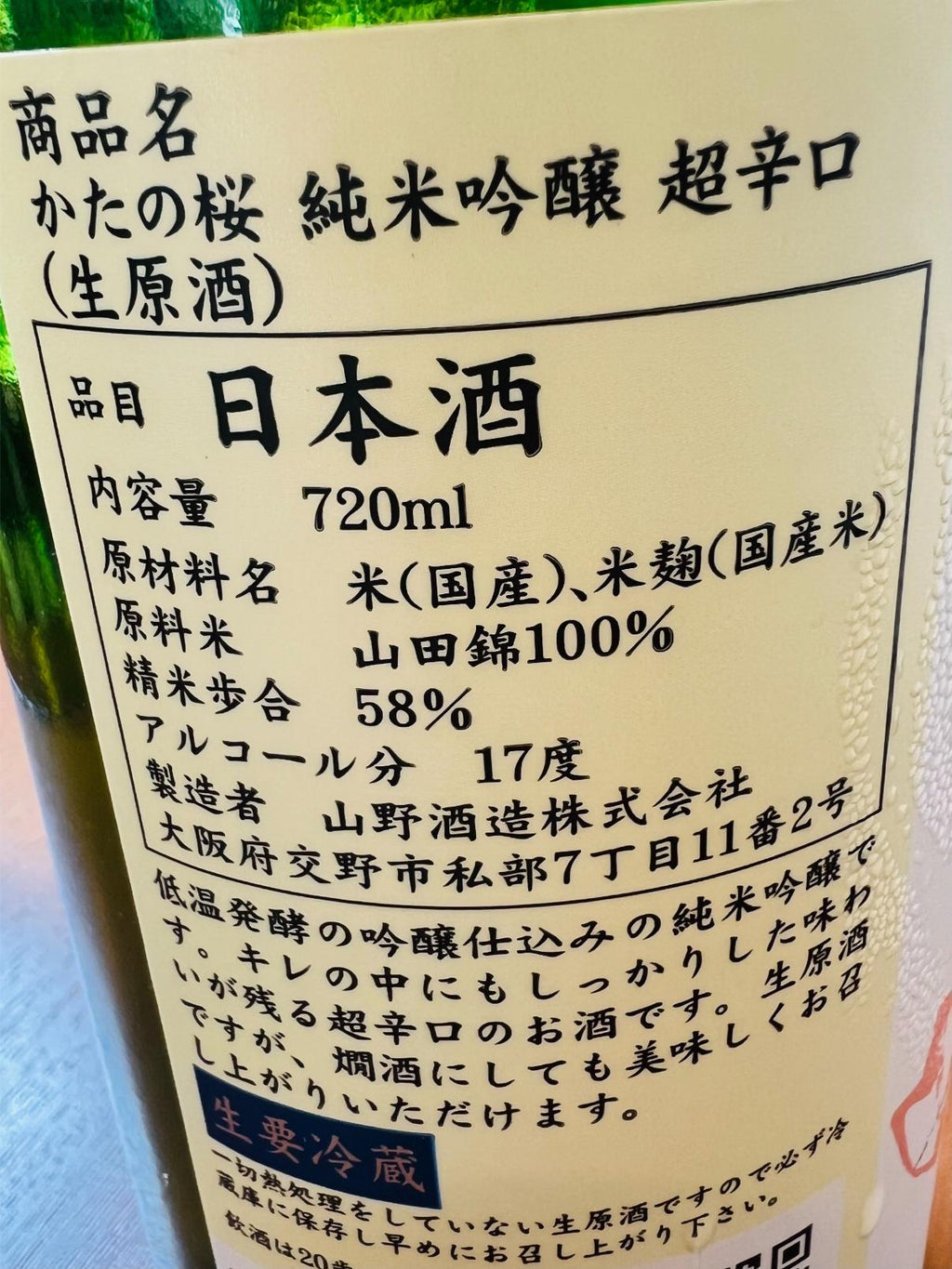 かたの桜 純米吟醸 超辛口 生原酒 720mlの裏面ラベル。大阪府交野市・山野酒造が山田錦を100％使用し、58％まで磨いて醸すアルコール17度の純米吟醸生原酒。低温発酵による吟醸仕込みで、キレの中にしっかりとした味わいが残る超辛口酒であることや、要冷蔵の表示を記載。
