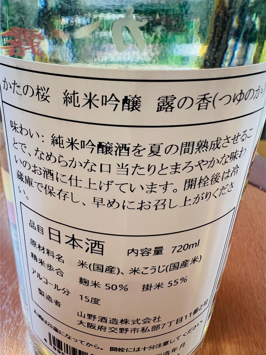 かたの桜 純米吟醸 露の香の裏面ラベル。大阪府交野市・山野酒造が醸す純米吟醸で、麹米50％・掛米55％まで精米し、アルコール15度。夏の間熟成させることで、なめらかな口当たりとまろやかな味わいに仕上げたことや、開栓後は冷蔵保存を推奨する旨が記載されている。