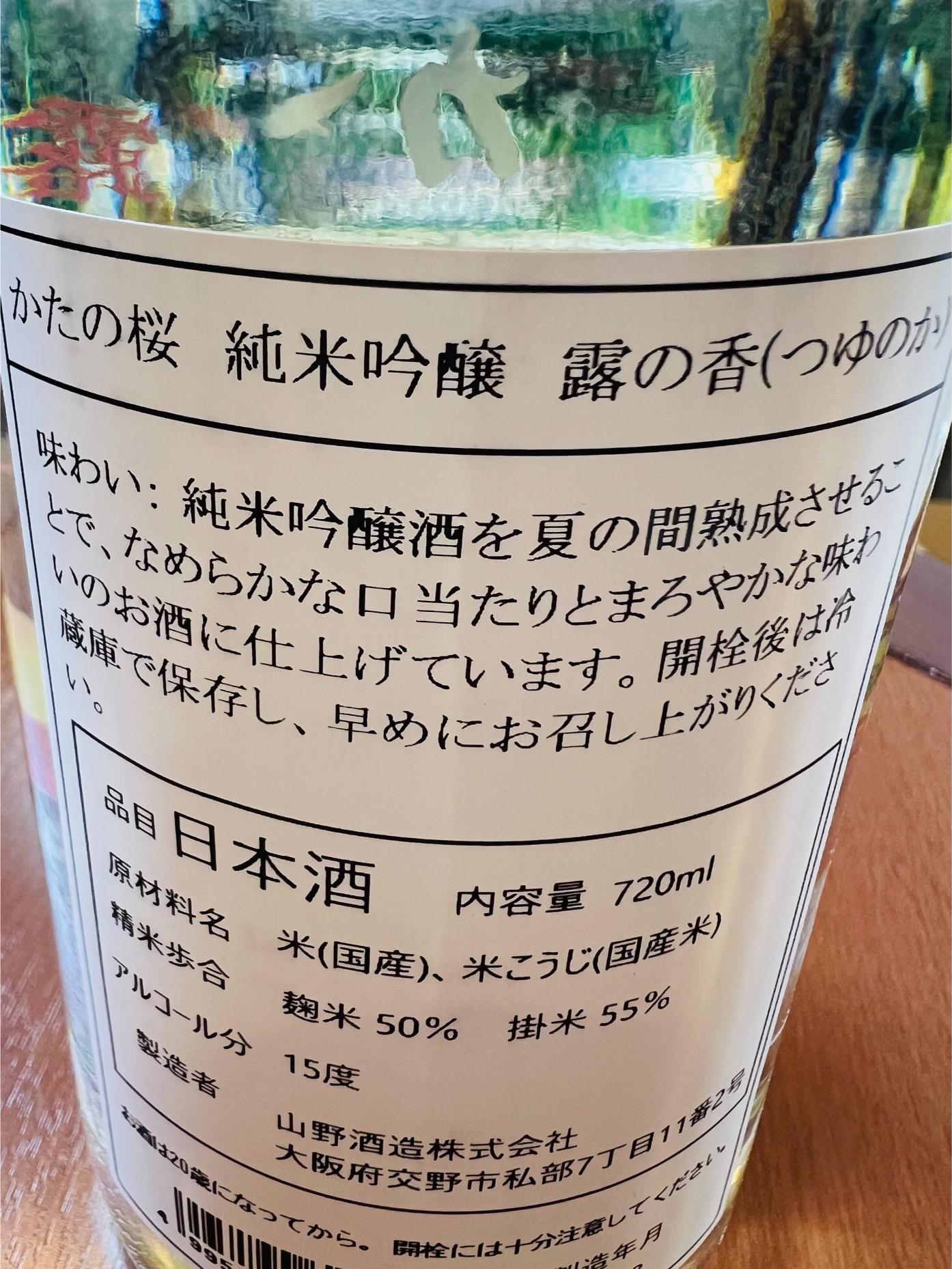 かたの桜 純米吟醸 露の香の裏面ラベル。大阪府交野市・山野酒造が醸す純米吟醸で、麹米50％・掛米55％まで精米し、アルコール15度。夏の間熟成させることで、なめらかな口当たりとまろやかな味わいに仕上げたことや、開栓後は冷蔵保存を推奨する旨が記載されている。