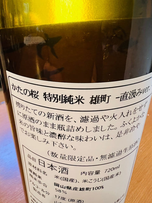大阪・山野酒造「かたの桜 特別純米 雄町 直汲みver.」の裏面ラベル詳細。搾りたての新酒を、濾過や火入れをせずに原酒のまま瓶詰めした無濾過生原酒の証が記されています。岡山県産「雄町」を100%使用し、精米歩合58%、アルコール分17度で仕上げた贅沢な造り。「ふくよかな米の旨味と濃醇な味わい」という蔵元の推奨通り、冷やして楽しむことで本領を発揮する、数量限定品の品質と情熱を伝える製品スペックです。