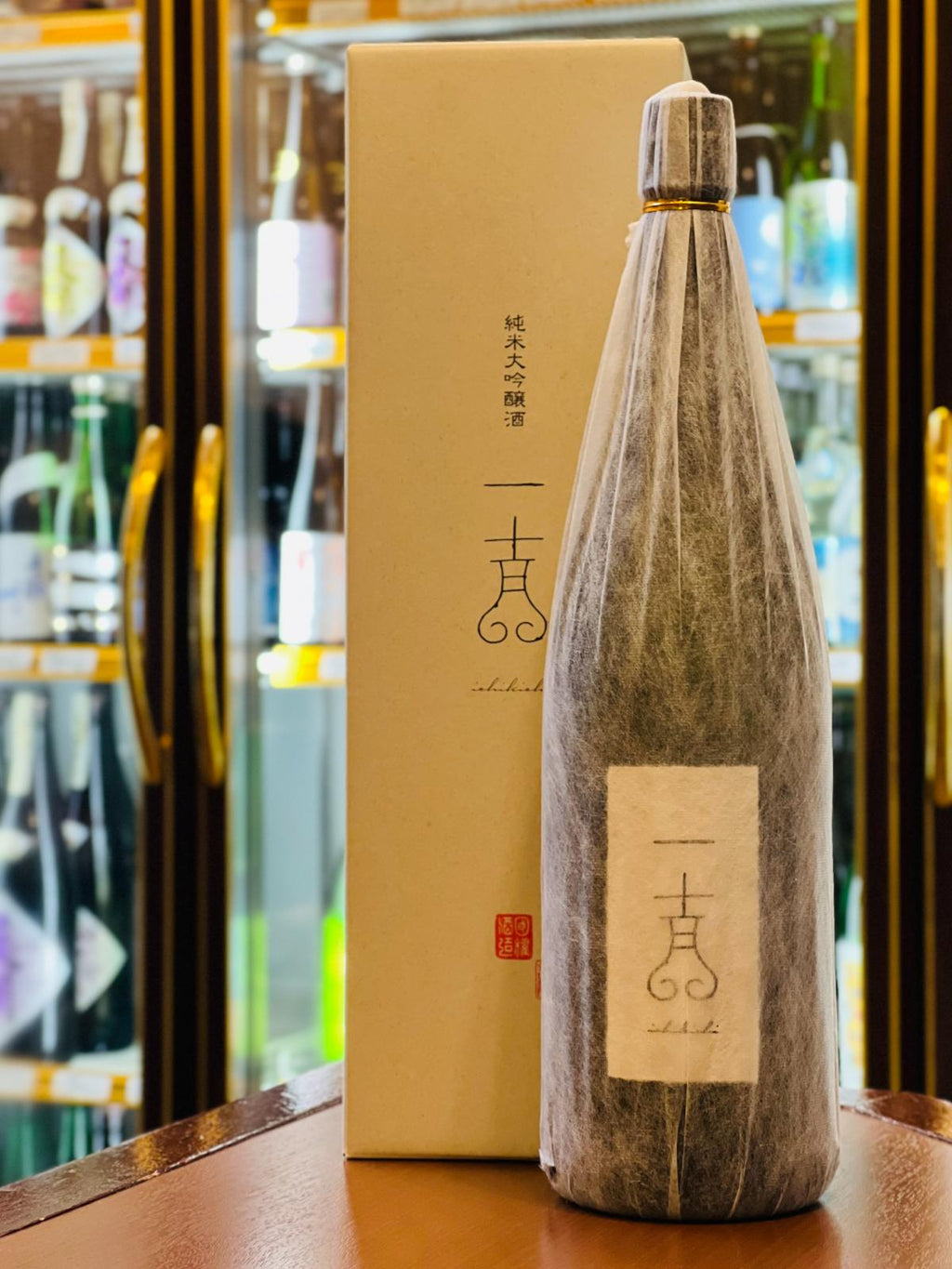 福島・国権酒造の最高級酒「純米大吟醸 一吉（いちきち） 1800ml」。清潔感のある白い和紙ラベルを施したボトルと、同じく白地のシンプルな化粧箱。桃や梨のような可憐でやさしい香りと、超軟水仕込みによる「さらさら・ふわふわ」とした滑らかな舌触りが特徴。凛とした佇まいの中に酒本来の旨みが宿る、気品溢れる逸品。