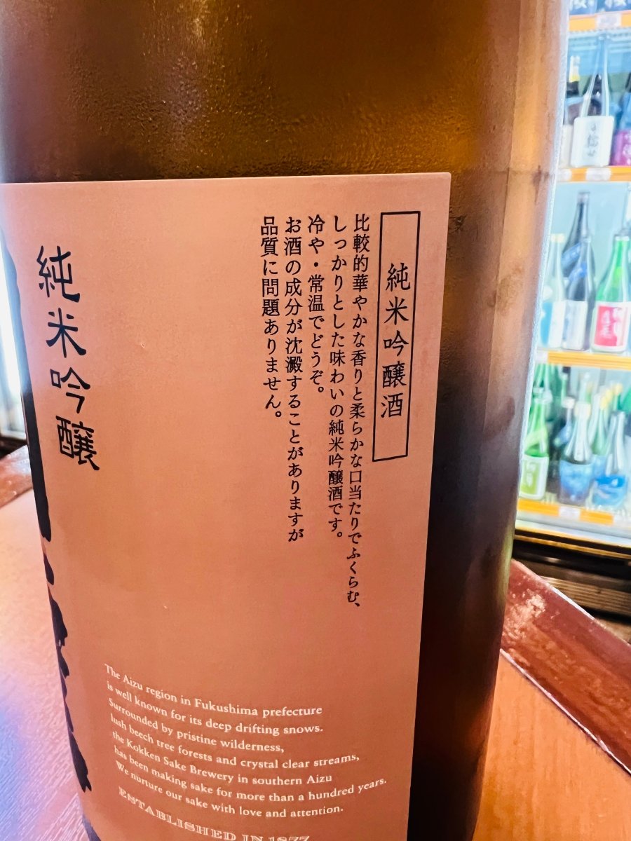 「国権 純米吟醸 銅ラベル」のラベル側面。「比較的華やかな香りと柔らかな口当たり」といった味わいの紹介や推奨温度（冷や・常温でどうぞ）が記されています。また、下部には福島県・南会津の美しい自然環境と、100年以上の歴史を持つ国権酒造の酒造りへの情熱が綴られた英文のメッセージが掲載されています。