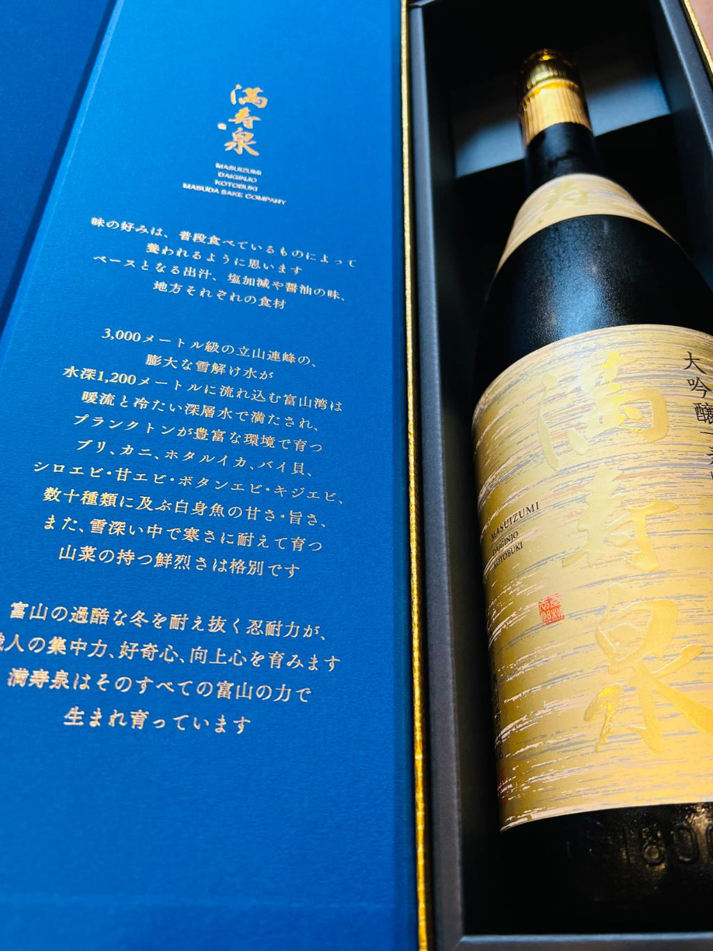 満寿泉 大吟醸 寿 1800mlの化粧箱を開けた状態。青色の内箱に富山の風土や食文化についての説明が記され、金色を基調としたボトルが収められている、贈答向け商品の詳細画像。