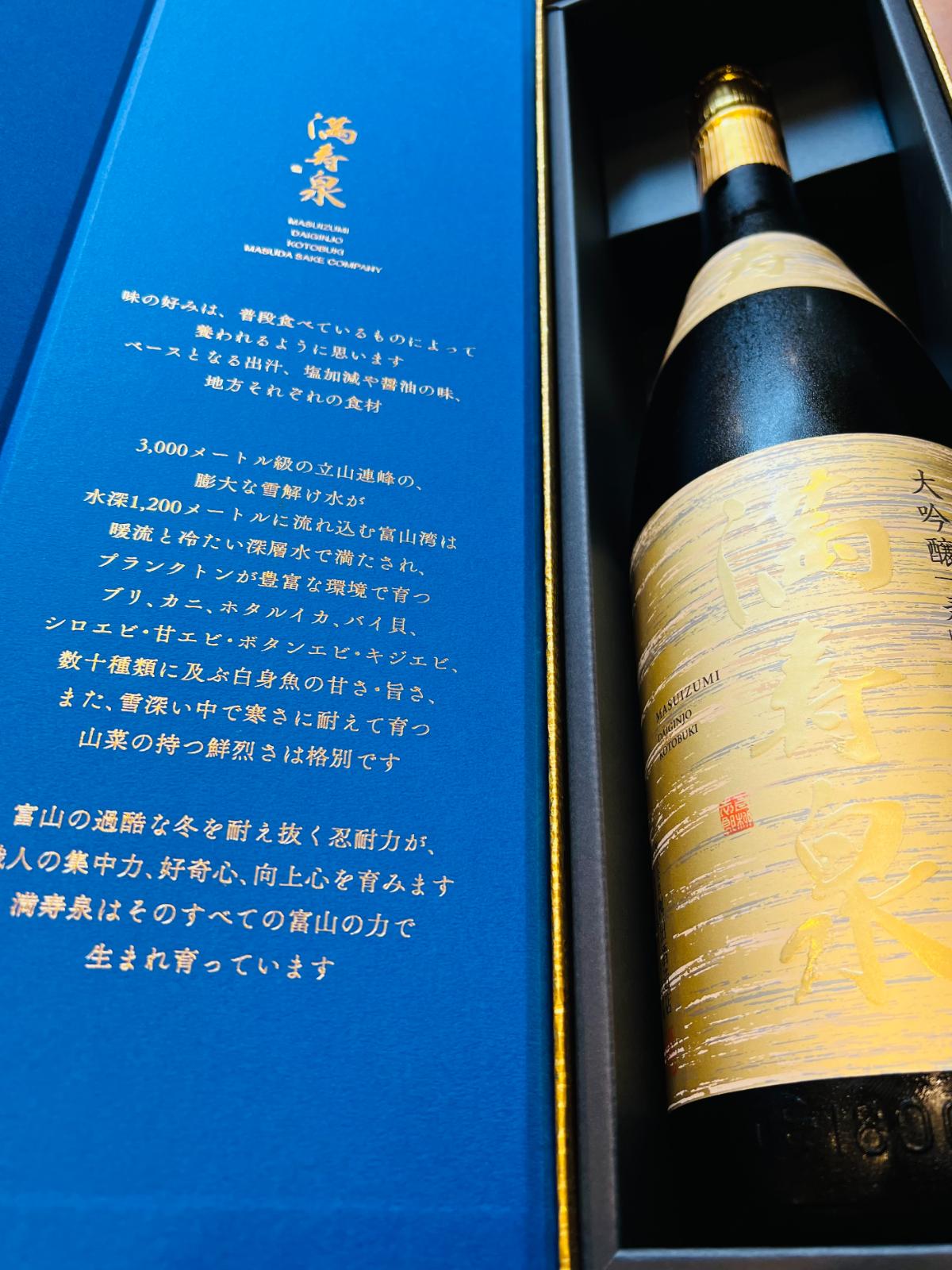 満寿泉 大吟醸 寿 1800mlの化粧箱を開けた状態。青色の内箱に富山の風土や食文化についての説明が記され、金色を基調としたボトルが収められている、贈答向け商品の詳細画像。