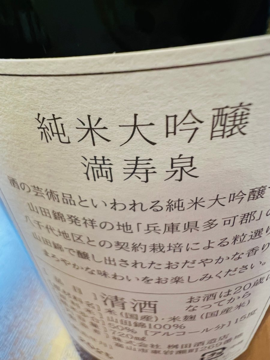 「満寿泉 純米大吟醸」720mlボトルの裏面ラベル。原材料の米、米麹ともに国産、精米歩合50％、アルコール分15度といった詳細スペックが記載されています。ラベル上部には「酒の芸術品」と称される由縁である、兵庫県多可郡八千代地区の契約栽培・山田錦を100％使用しているこだわりが記されています。