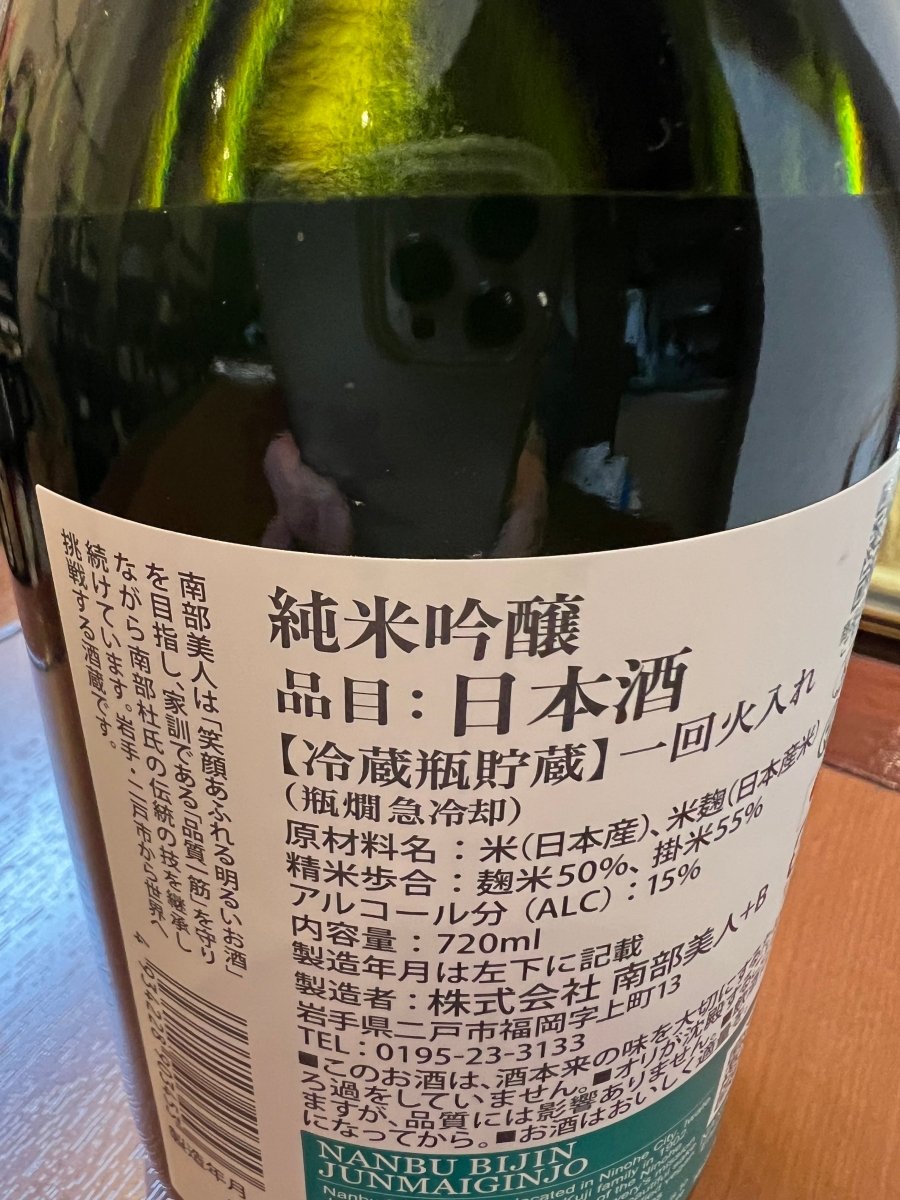 「南部美人 純米吟醸」の裏面ラベル。精米歩合（麹米50%・掛米55%）やアルコール分15%などの詳細スペックに加え、鮮度を保つための「冷蔵瓶貯蔵」と「一回火入れ（瓶燗急冷却）」のこだわりが記されています。家訓である「品質一筋」を守り、南部杜氏の伝統の技で醸された、優しく華やかでエレガントな味わいを支える品質表示の画像です。