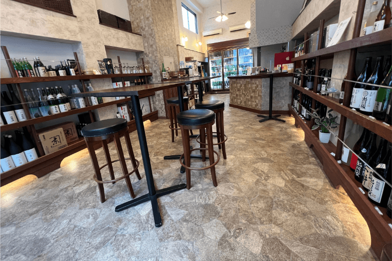 地酒専門店 酒逢店内の落ち着いた雰囲気・木目調の内装。試飲ができるテーブルとカウンター。奥に冷蔵庫。