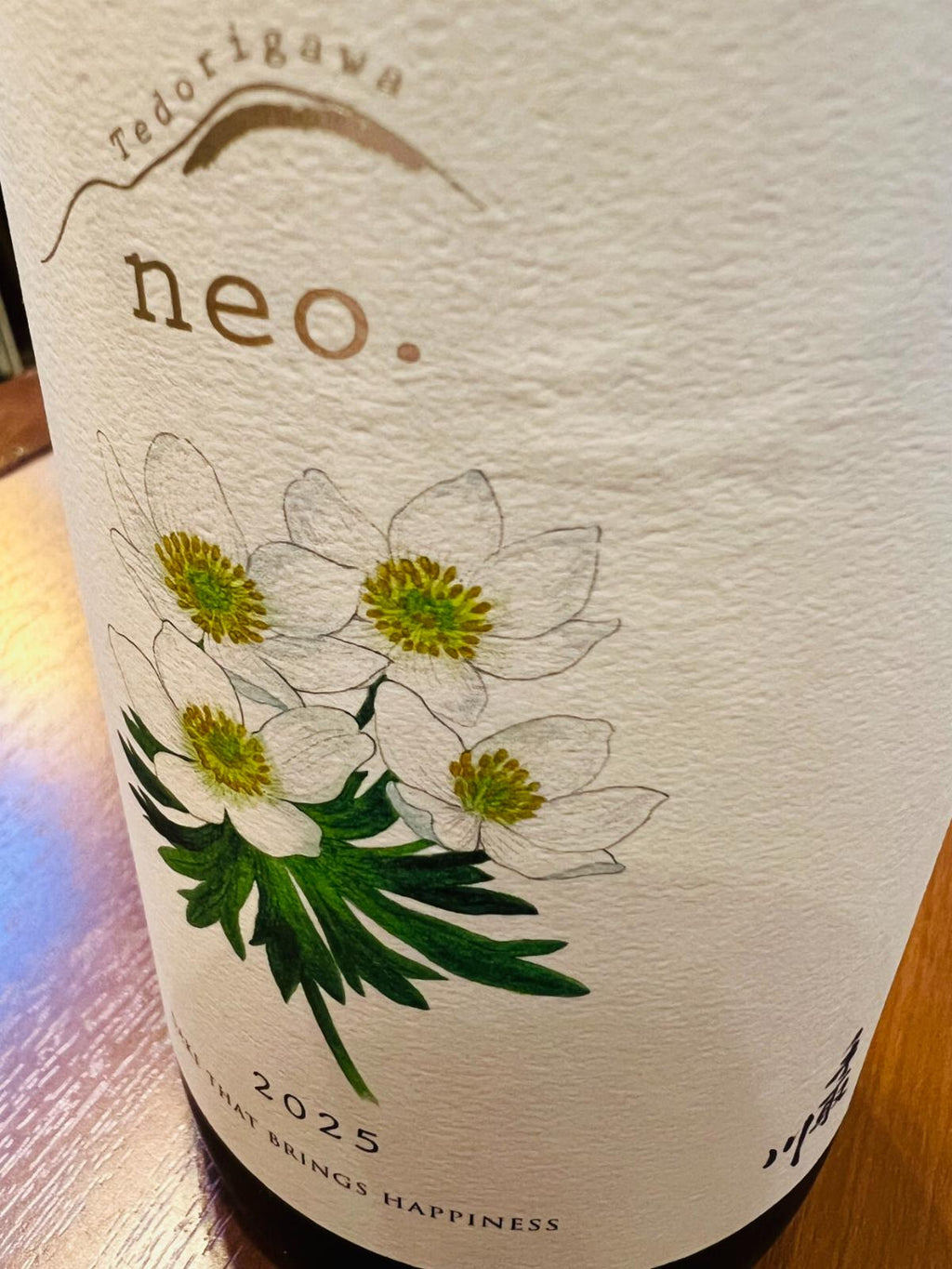 手取川 neo. 2025 SAKE THAT BRINGS HAPPINESSのラベル接写。生成り色のラベルに「neo.」「2025」「SAKE THAT BRINGS HAPPINESS」の文字と、白山の高山植物ハクサンイチゲの花が描かれている。