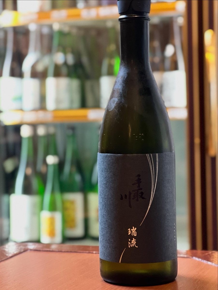 石川・吉田酒造店の最高峰「手取川 瑞流（ずいりゅう）」720mlボトル。黒いマットな瓶に、白山の雪解け水の流れをイメージした流麗なラインが描かれた、気品溢れる佇まいの一本です。石川県産「百万石乃白」を40％まで磨き、伝統の山廃造りで醸されたこのお酒は、高級な桃を思わせる透明感ある果実味と、さらさらとしたシルキーな口当たりが魅力。特別な日のための至高の一本です。
