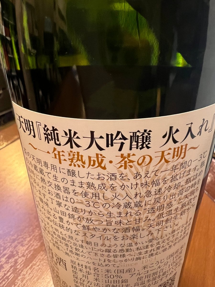 福島・曙酒造「純米大吟醸 一年熟成・茶の天明」の裏ラベル詳細。生のまま一年間0-3℃で熟成させて味幅を広げ、瓶詰め時に熱交換器で火入れ急冷するという、手間暇かけた製法が記されています。丁寧な造りから生まれる透明感、山田錦の旨味と甘み、そして天明らしい酸味が調和した、伝統的なスタイルを伝えるラベル画像です。