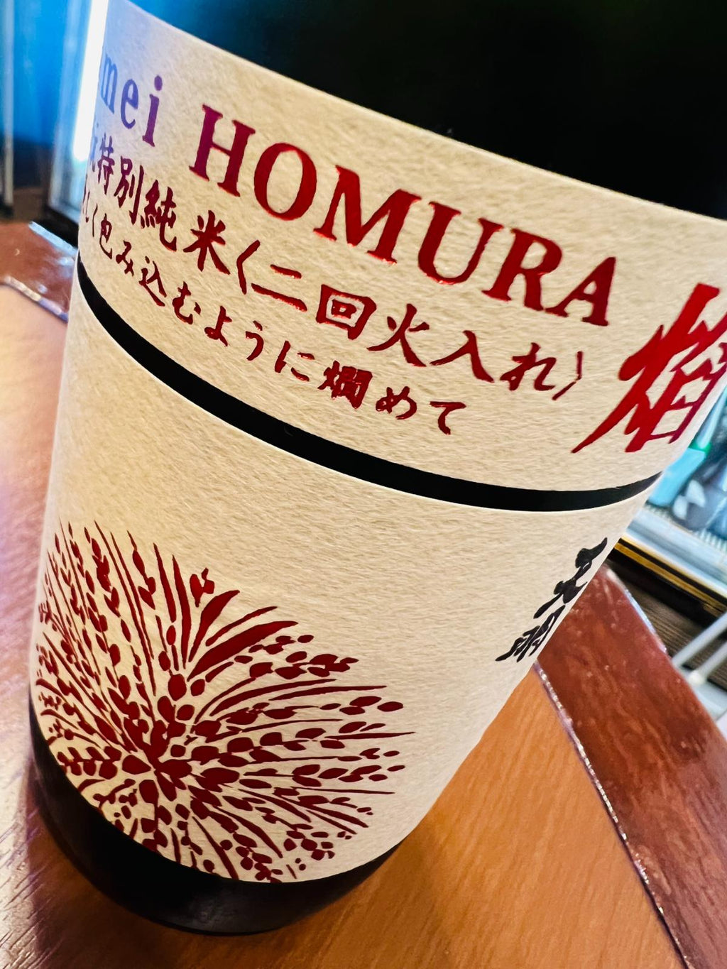 tenmei 焔 HOMURA 山廃酛 特別純米 二回火入のラベル接写。生成り色のラベルに赤字で「tenmei HOMURA 焔」、山廃酛特別純米・二回火入の表記が入り、下部には赤い稲穂を思わせる意匠が描かれている。