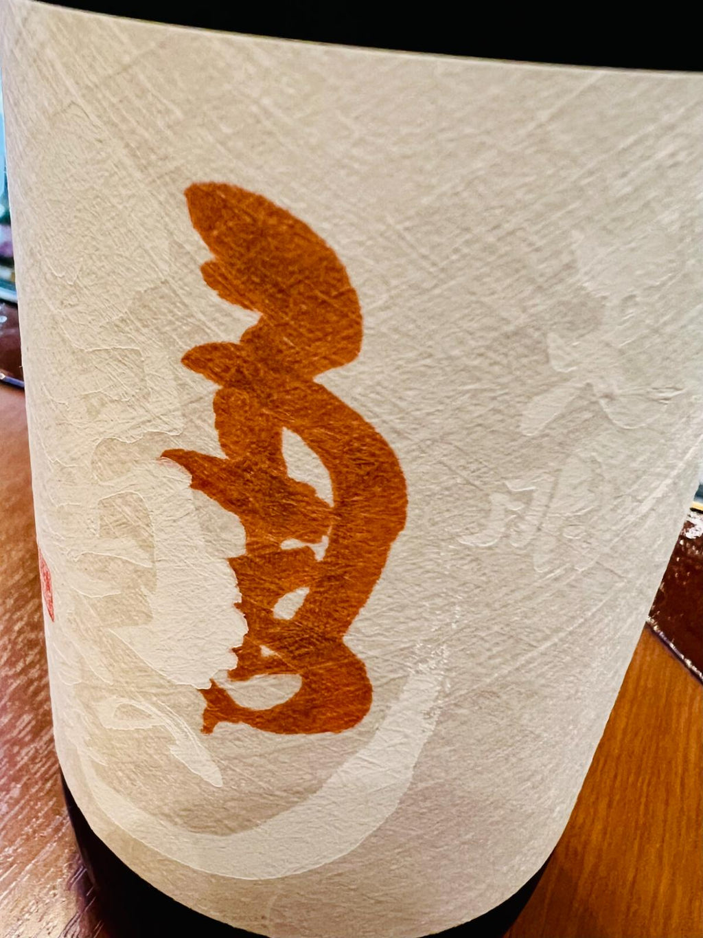 天明 純米 亀の尾 二回火入のラベル接写。白地の和紙調ラベルに、橙色で「天明」と「亀の尾」を崩した意匠が重ねて描かれたデザイン。